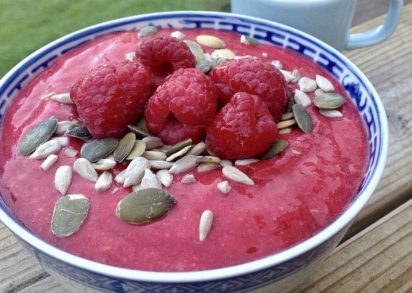 Skål med raw banan och hallonkräm toppad med fröer och färska hallon