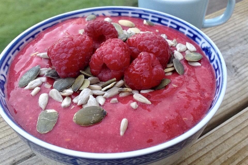 Skål med raw banan och hallonkräm toppad med fröer och färska hallon