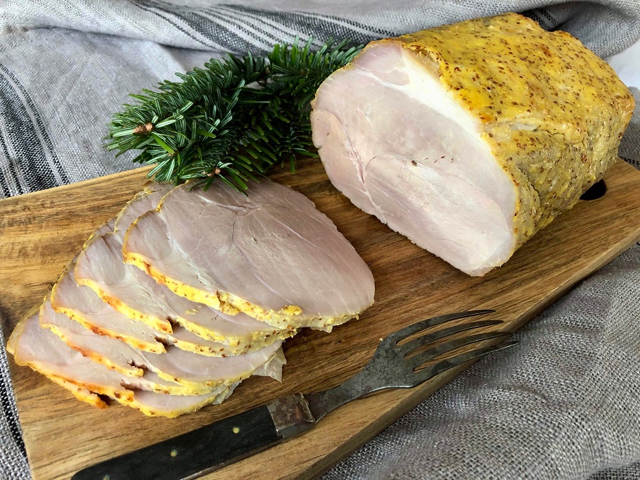 Uppskuren senapsgriljerad julskinka på ett träfat.
