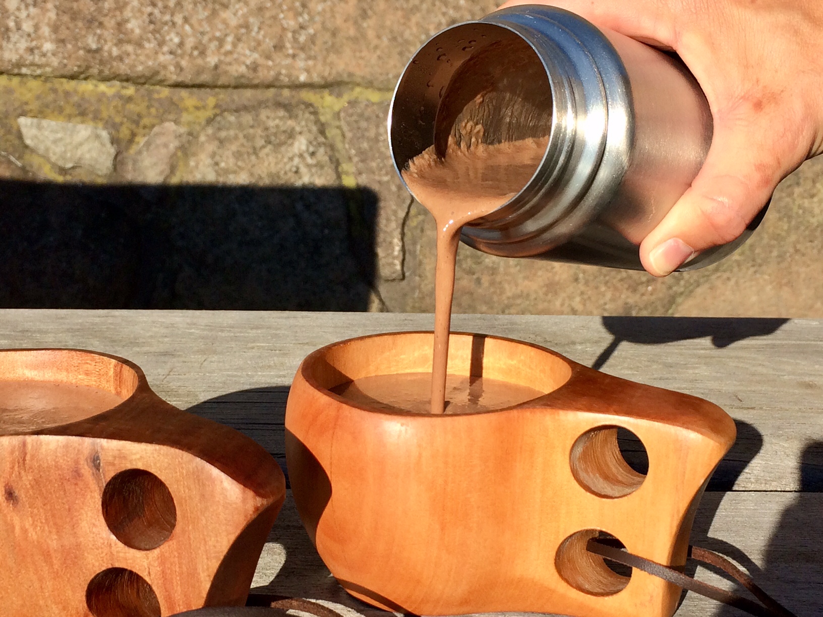 Häller upp varm choklad från en termos i träkåsor