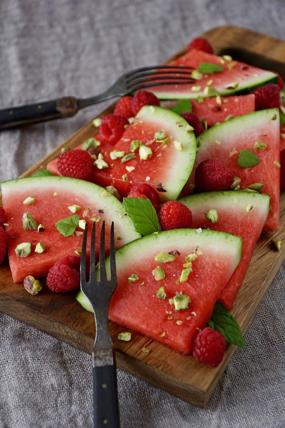 Närbild på vattenmelon, hallon, pistagenötter och mynta på en skärbräda