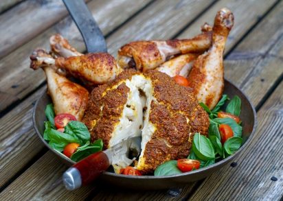 Helrostad blomkål i en stekpanna tillsammans med grillade kycklingben och sallad