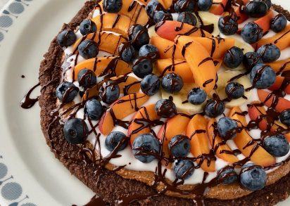 Ljuvlig Efterrättspizza med en choklad brownie botten toppad med mandelsmör, fräsch kokosyoghurt, frukt och bär.