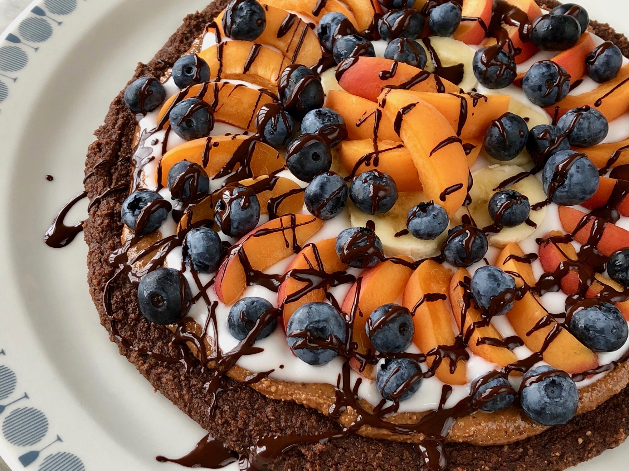 Ljuvlig Efterrättspizza med en choklad brownie botten toppad med mandelsmör, fräsch kokosyoghurt, frukt och bär.